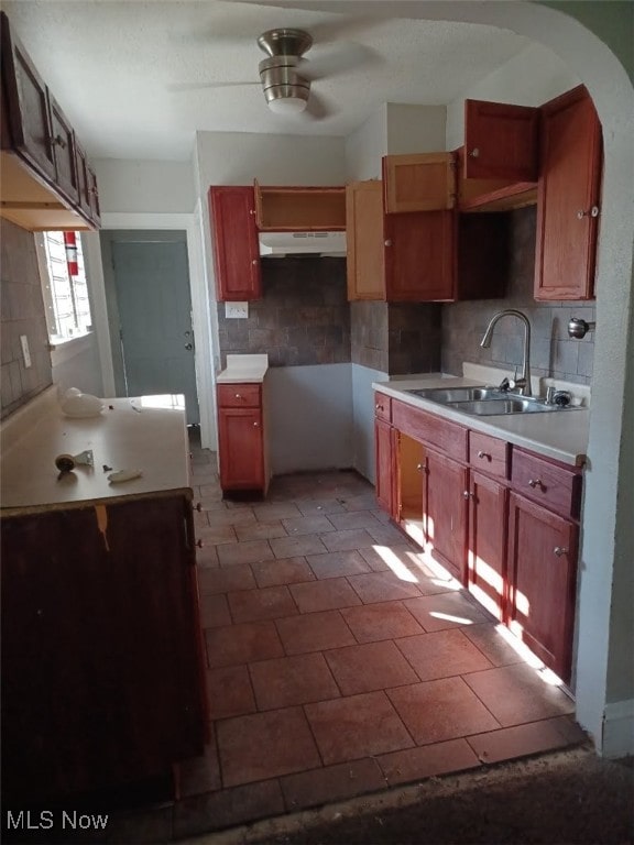 kitchen featuring under cabinet range hood, decorative backsplash, arched walkways, a ceiling fan, and a sink