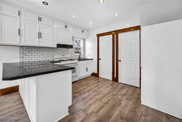 kitchen featuring wood finished floors, white gas range oven, a peninsula, exhaust hood, and white cabinets