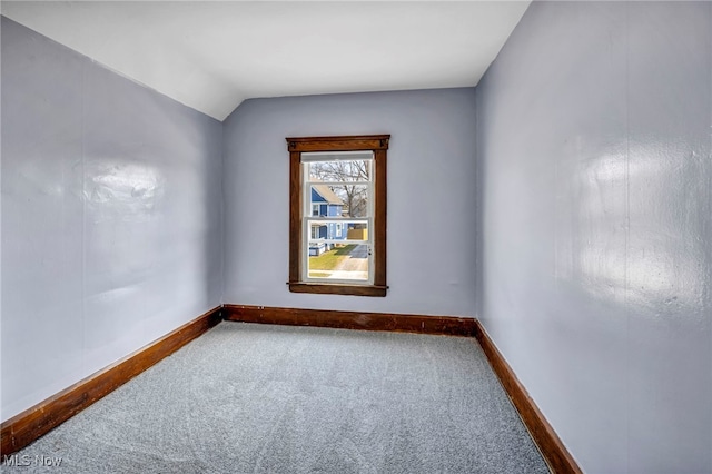 carpeted spare room featuring baseboards and vaulted ceiling