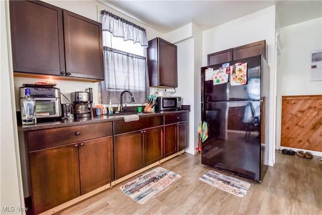 kitchen featuring dark countertops, stainless steel microwave, freestanding refrigerator, light wood-style floors, and a sink