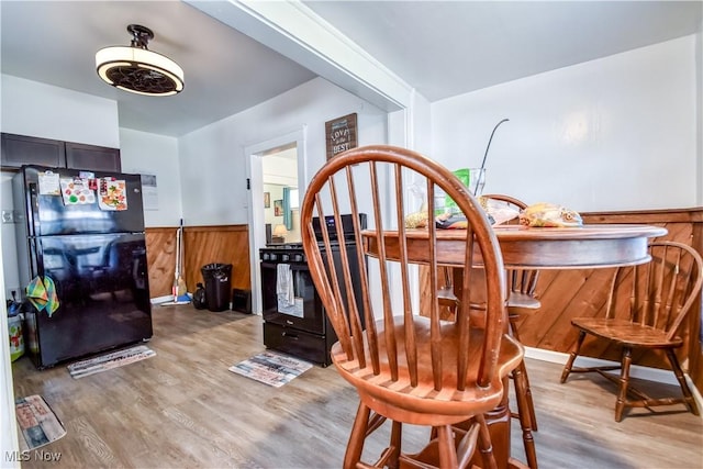 dining area featuring light wood-type flooring, wood walls, and wainscoting