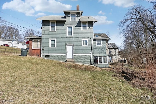 rear view of property featuring a yard, a chimney, and fence