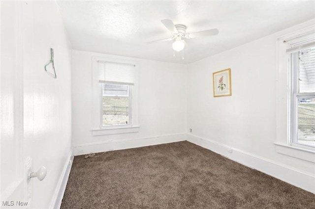 empty room featuring dark carpet, baseboards, a healthy amount of sunlight, and ceiling fan