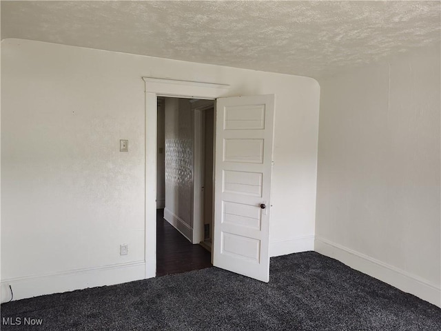 empty room featuring baseboards, dark carpet, and a textured ceiling