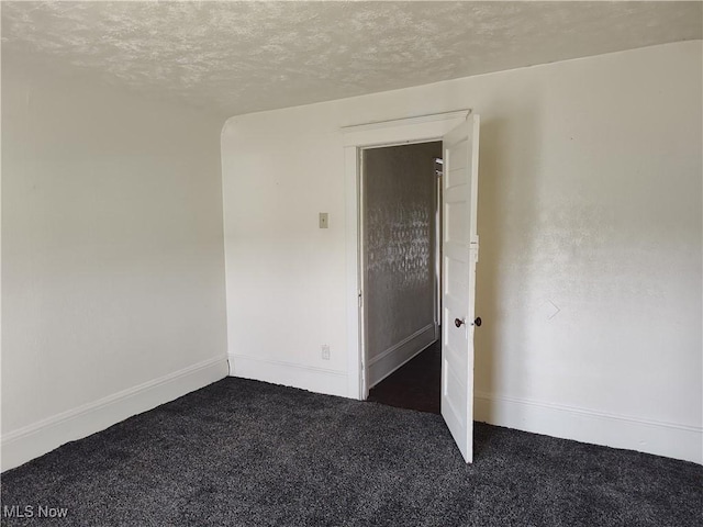 spare room featuring dark carpet, a textured ceiling, and baseboards