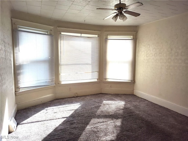 carpeted spare room featuring a textured wall, baseboards, and ceiling fan