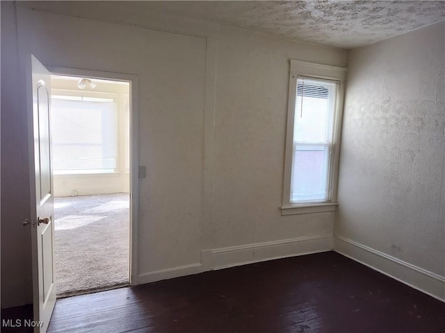 empty room with a textured ceiling, dark wood-type flooring, baseboards, and a textured wall