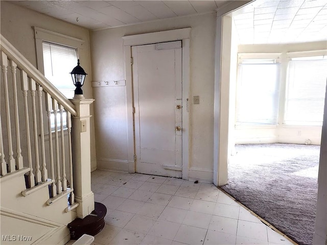 foyer featuring stairway, light carpet, and baseboards