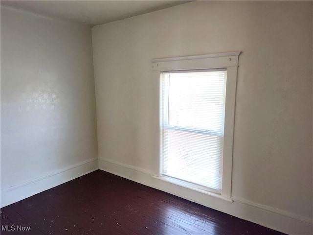 spare room featuring baseboards and dark wood-type flooring