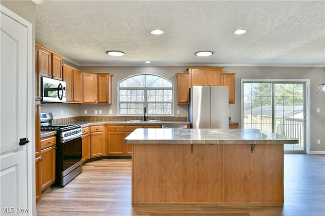 kitchen with a healthy amount of sunlight, a kitchen island, light wood-style flooring, a sink, and stainless steel appliances