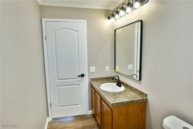 half bathroom featuring toilet, wood finished floors, crown molding, baseboards, and vanity