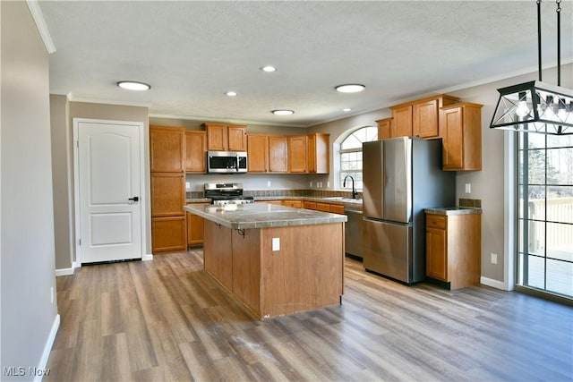 kitchen featuring a kitchen island, a sink, light wood-style floors, appliances with stainless steel finishes, and crown molding