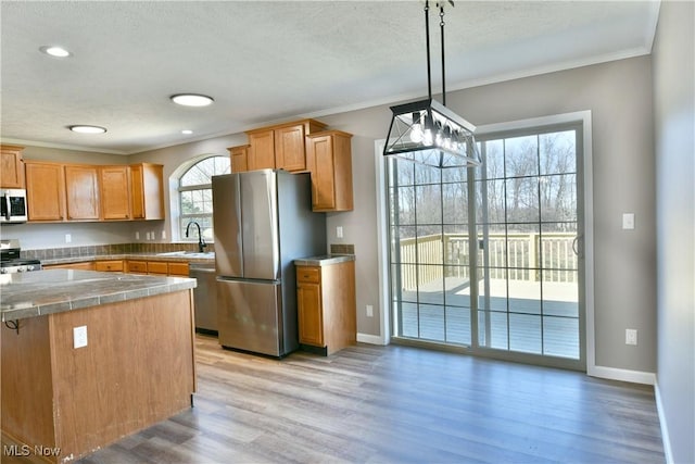 kitchen featuring crown molding, baseboards, light wood-style floors, stainless steel appliances, and a sink