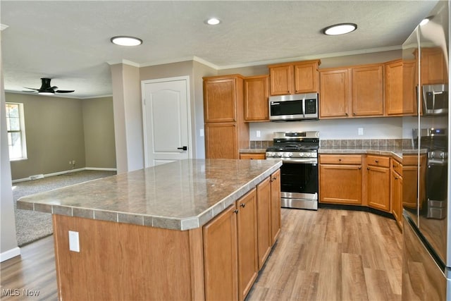 kitchen with light wood finished floors, a kitchen island, crown molding, ceiling fan, and stainless steel appliances