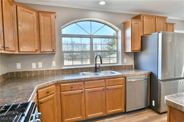 kitchen with light wood finished floors, crown molding, brown cabinetry, stainless steel appliances, and a sink