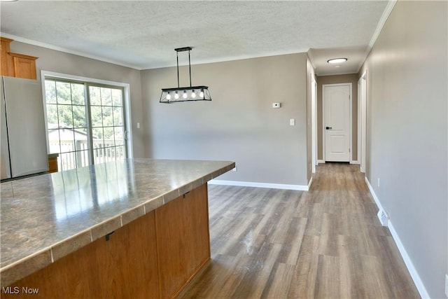 kitchen featuring crown molding, baseboards, freestanding refrigerator, brown cabinetry, and a textured ceiling