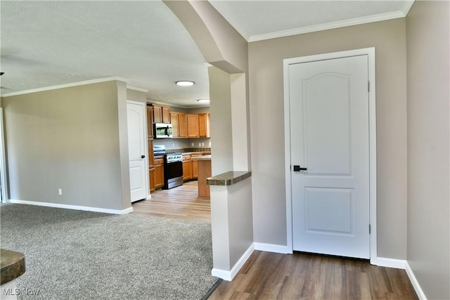 kitchen with brown cabinets, ornamental molding, stainless steel appliances, carpet, and baseboards