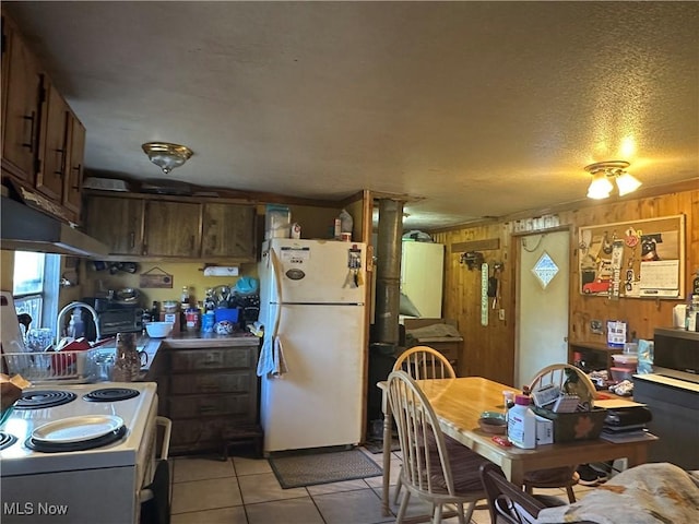 kitchen featuring a textured ceiling, white appliances, light tile patterned floors, under cabinet range hood, and wood walls