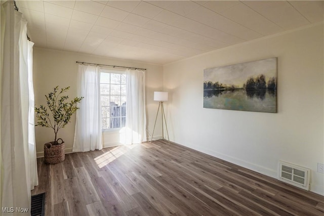 empty room with visible vents, baseboards, wood finished floors, and crown molding