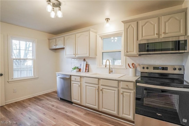 kitchen with light wood finished floors, backsplash, light countertops, appliances with stainless steel finishes, and a sink