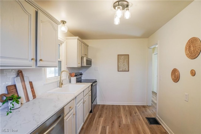 kitchen with visible vents, light wood-style flooring, a sink, stainless steel appliances, and baseboards