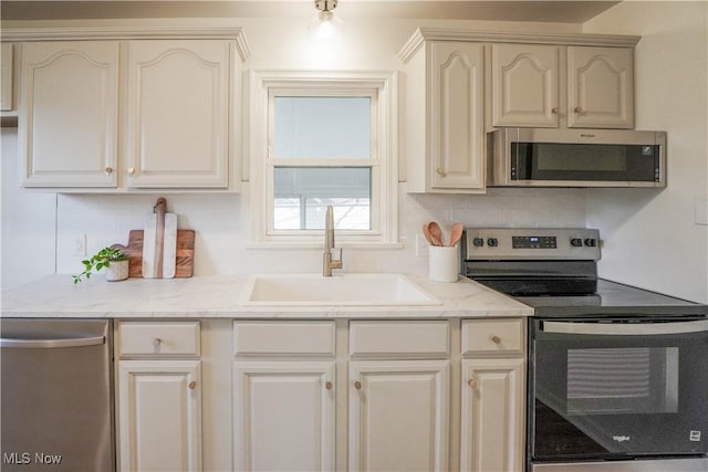 kitchen with cream cabinetry, a sink, tasteful backsplash, appliances with stainless steel finishes, and light stone countertops