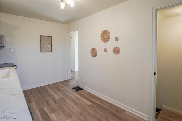 unfurnished dining area featuring visible vents, light wood-style flooring, baseboards, and a sink