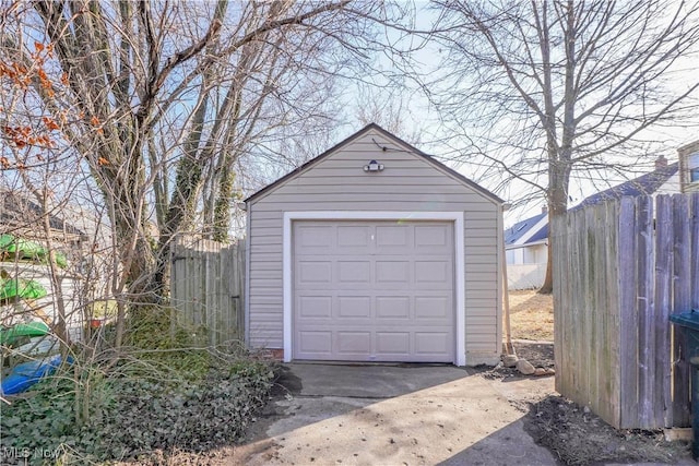 detached garage featuring concrete driveway and fence