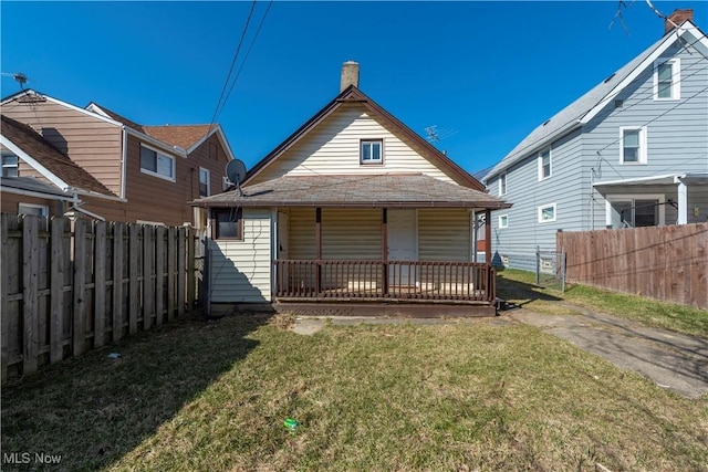 back of house featuring a porch, a chimney, a yard, and fence