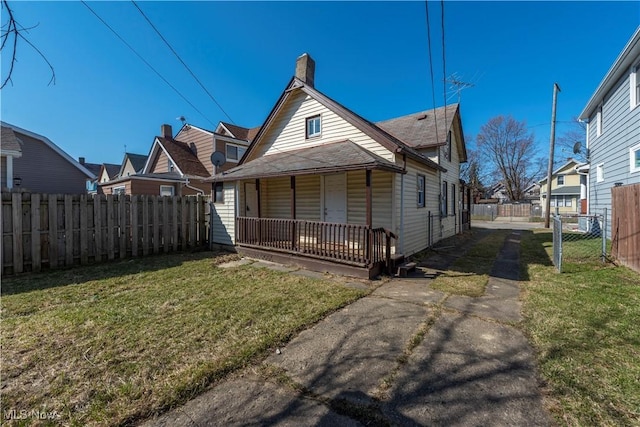 rear view of house with fence, covered porch, a lawn, a chimney, and driveway