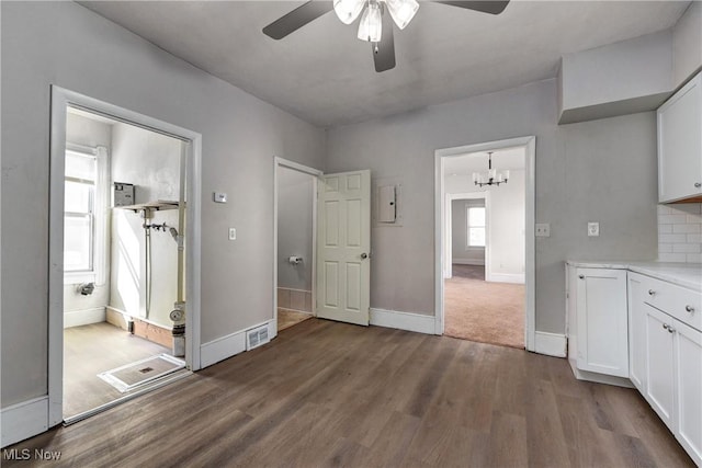 unfurnished bedroom with dark wood finished floors, visible vents, ceiling fan with notable chandelier, and baseboards