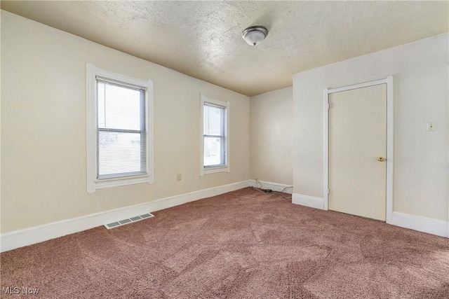 carpeted spare room with visible vents, baseboards, and a textured ceiling