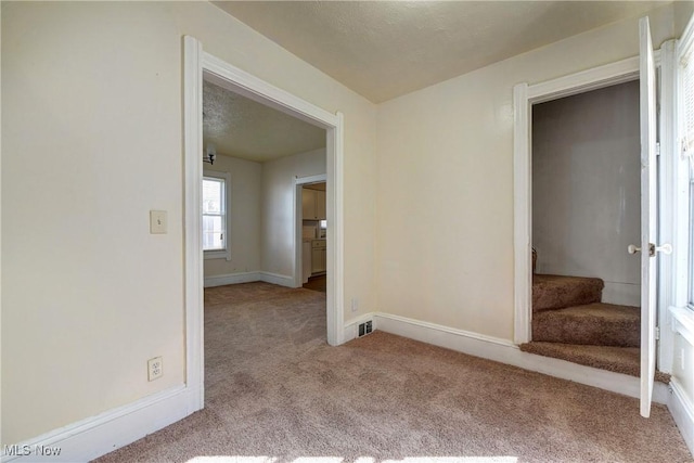 empty room featuring carpet flooring, stairway, a textured ceiling, and baseboards