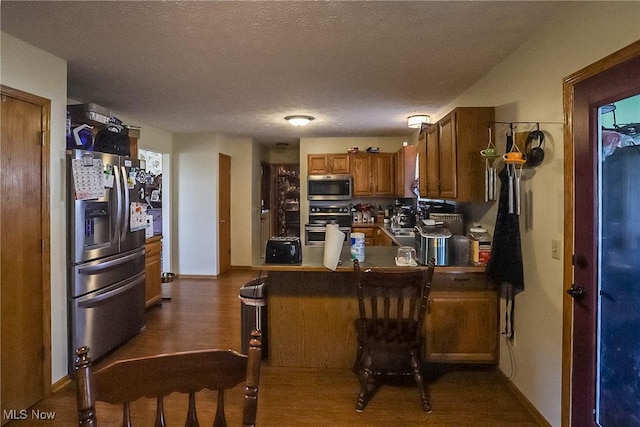 kitchen featuring a peninsula, stainless steel appliances, dark wood-type flooring, a textured ceiling, and brown cabinets