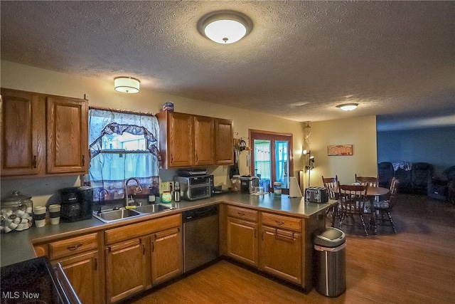 kitchen with wood finished floors, a peninsula, a sink, stainless steel dishwasher, and brown cabinets