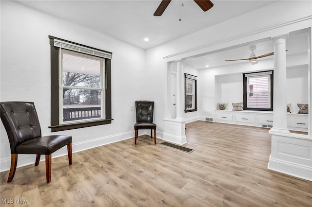 living area with a ceiling fan, light wood-style floors, and ornate columns