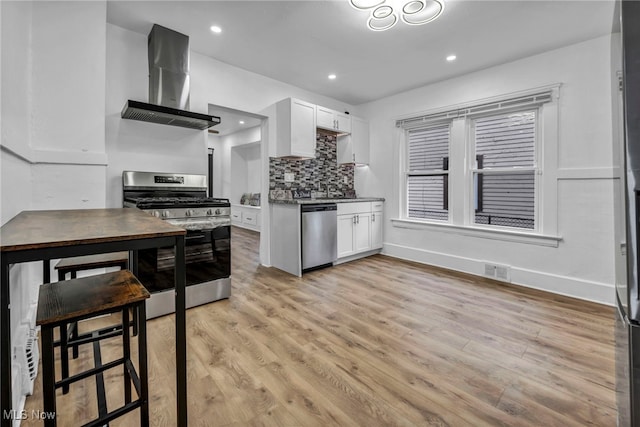 kitchen featuring light wood-style flooring, appliances with stainless steel finishes, wall chimney exhaust hood, and white cabinets