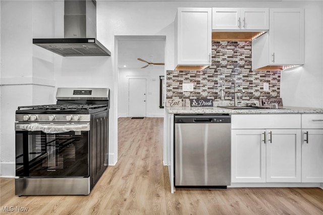 kitchen featuring light wood-type flooring, decorative backsplash, appliances with stainless steel finishes, white cabinets, and wall chimney exhaust hood