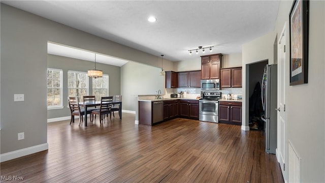 kitchen featuring appliances with stainless steel finishes, dark wood-type flooring, a peninsula, and a sink