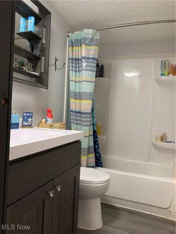 bathroom with toilet, shower / bath combo, a textured ceiling, wood finished floors, and vanity