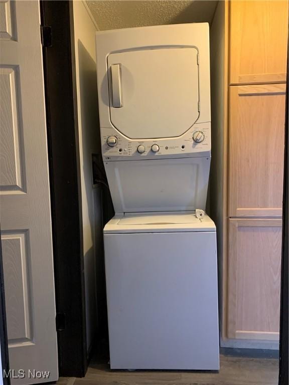 clothes washing area with a textured ceiling, stacked washer and clothes dryer, wood finished floors, and laundry area