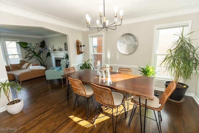 dining room with baseboards, ornamental molding, a fireplace, dark wood-style floors, and a notable chandelier