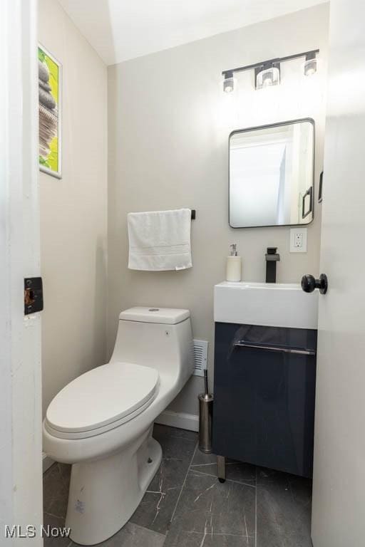 half bath with baseboards, toilet, marble finish floor, and vanity