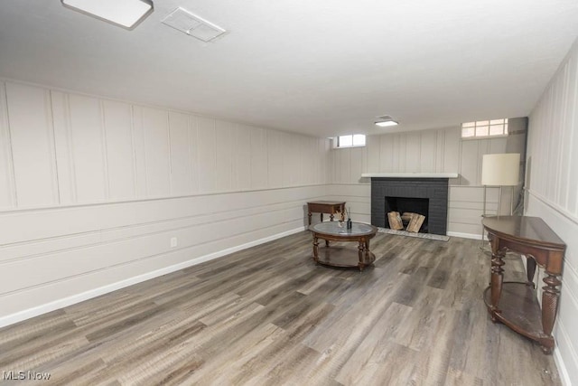 living area featuring baseboards, a brick fireplace, and wood finished floors