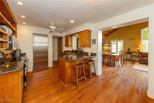 kitchen featuring vaulted ceiling, appliances with stainless steel finishes, a peninsula, wood finished floors, and a baseboard radiator