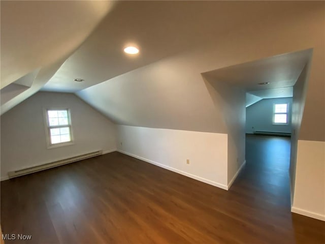 additional living space with a baseboard heating unit, wood finished floors, a healthy amount of sunlight, and lofted ceiling