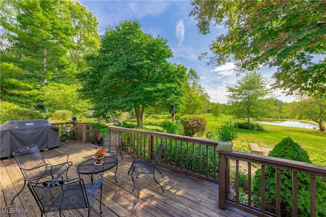 wooden terrace featuring grilling area, a water view, and a yard