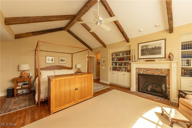 bedroom featuring lofted ceiling with beams, a brick fireplace, wood finished floors, and baseboards