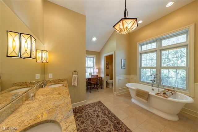 full bathroom with toilet, a sink, wainscoting, a decorative wall, and a soaking tub