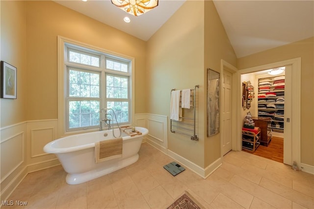 bathroom featuring a spacious closet, lofted ceiling, wainscoting, a freestanding tub, and a decorative wall